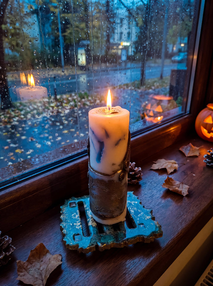 Lit Break the Seal beeswax candle on a resin stand by a rain-covered window, with autumn leaves and glowing jack-o’-lanterns.