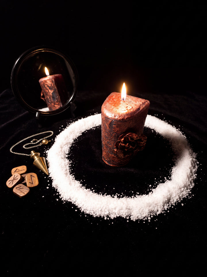 Corrosion candle burning inside a circle of salt beside a mirror, pendulum and rune stones