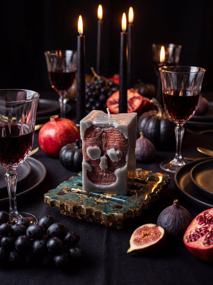 Unlit Inner Demon skull candle on a resin stand at a dark dining table with wine glasses, figs, pomegranates and taper candles.
