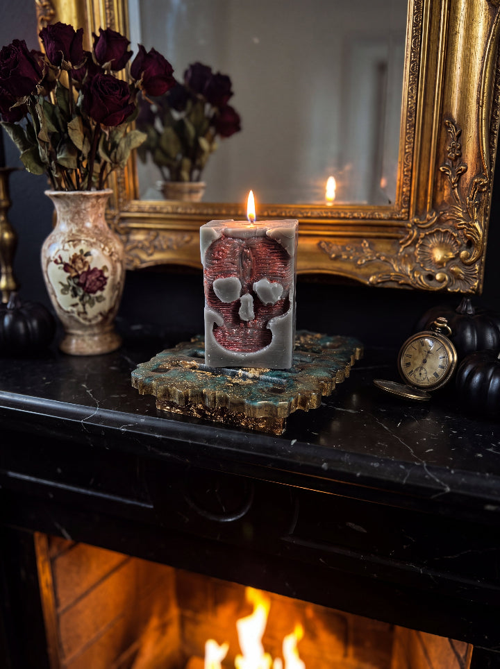 Lit Inner Demon skull candle on a resin stand above a fireplace, with an ornate gold mirror, dried roses and a vintage clock.