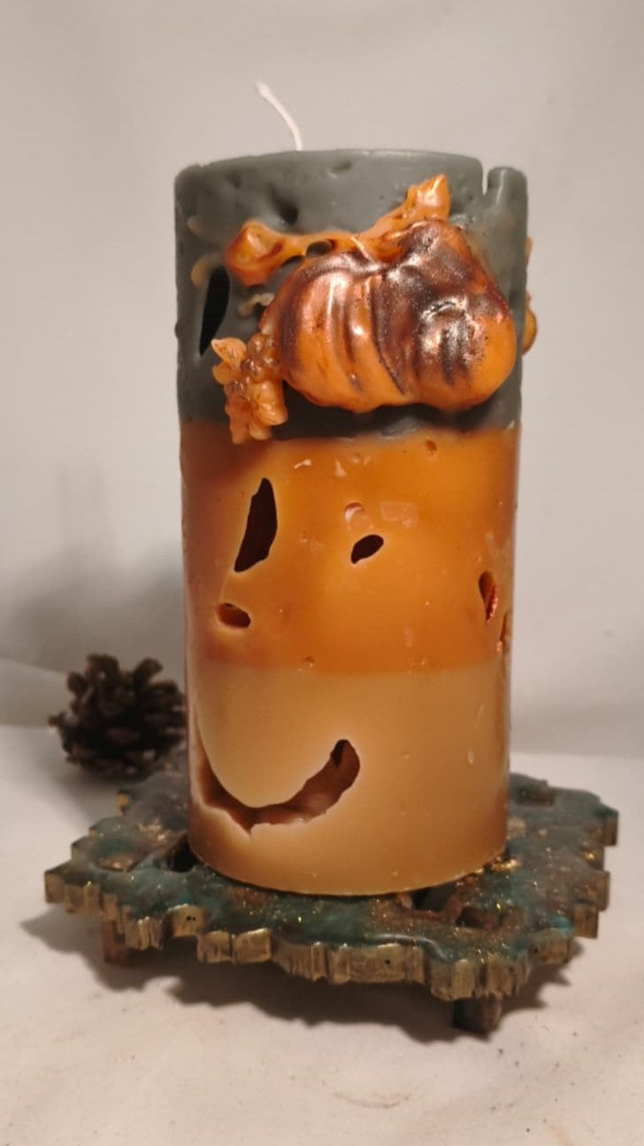 Close-up of Witch’s Harvest beeswax candle with a smiling face, raised pumpkin detail and dark green top.