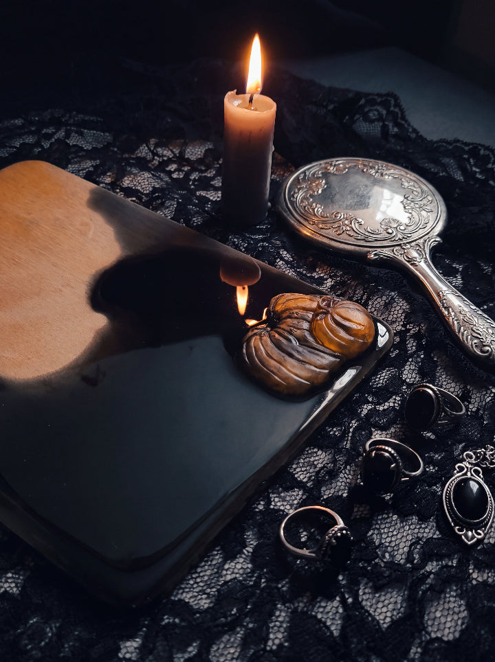 Close-up of Salem Board pumpkin resin detail beside a candle and silver mirror