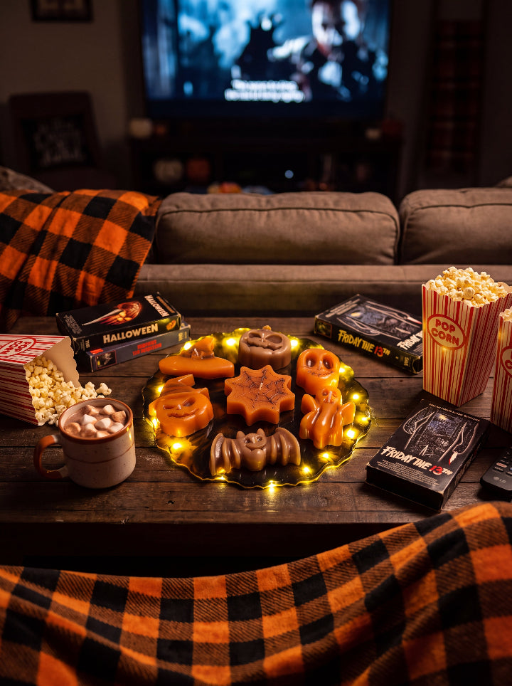 Spellbound Halloween candle set on a glowing resin stand on a coffee table with popcorn and hot chocolate for a horror movie night.