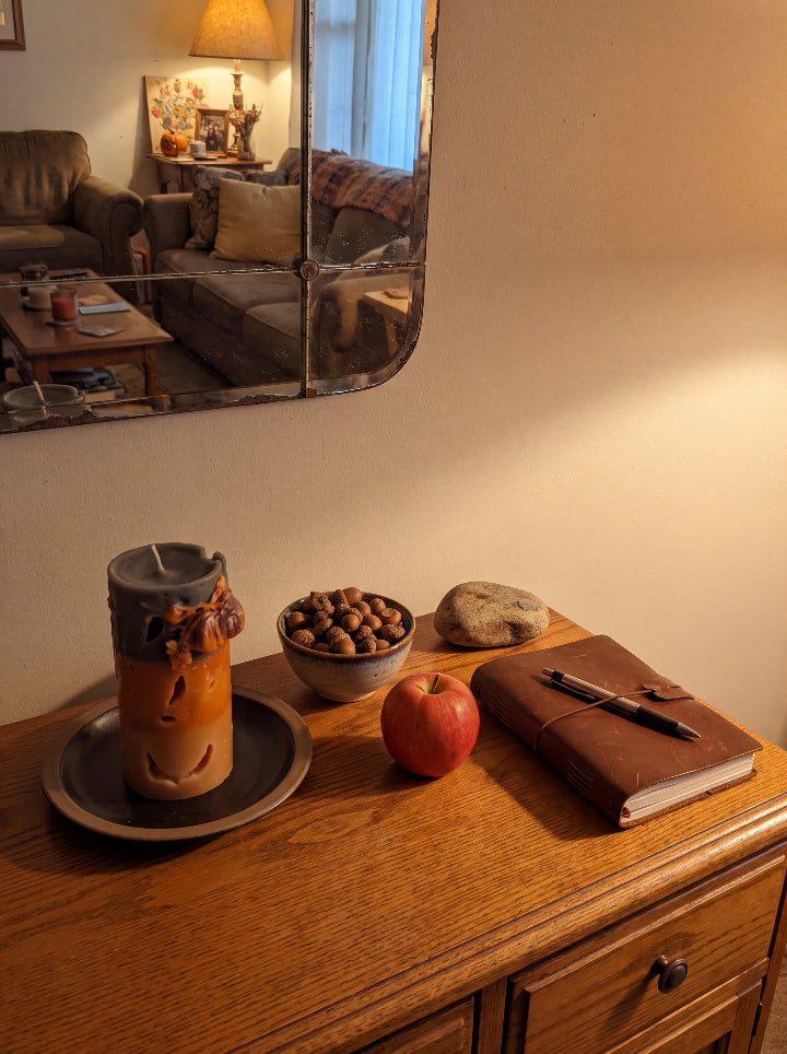 Witch’s Harvest candle on a wooden desk beside an apple, a bowl of nuts and a journal.