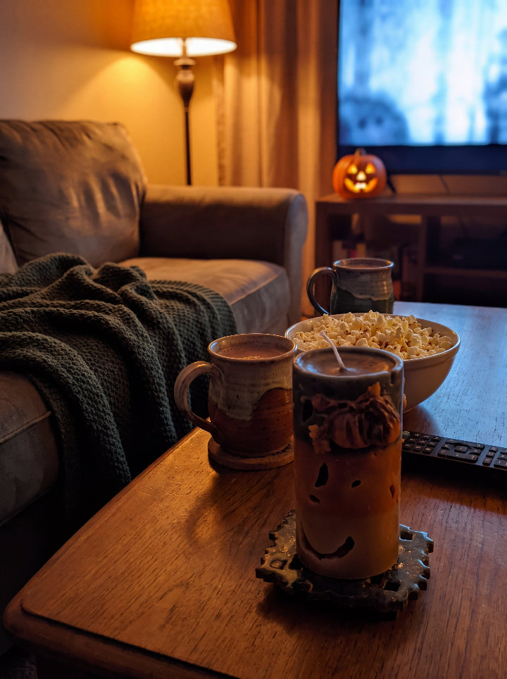 Witch’s Harvest candle on a coffee table with popcorn and mugs in a Halloween living room.